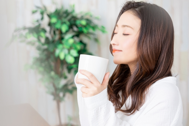 温かい飲み物を手に、目を閉じてほっとする女性